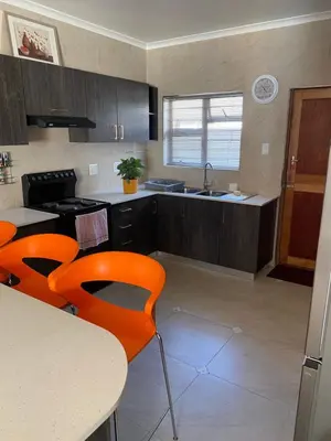 a kitchen with a table and orange chairs in it at Birds Nest Holiday Apartment in Zeekoevlei
