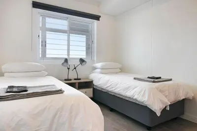 two beds in a white room with a window at Chic Beachfront Apt with Table Mountain Views Horizon Bay 902 in Cape Town