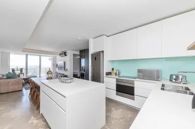 a kitchen with white cabinets and a living room at Modern Sea View Retreat with Pool & Inverter Horizon Bay 1405 in Cape Town