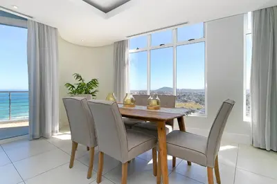 a dining room with a table and chairs and windows at Horizon Bay 1602 Penthouse APT with lovely views in Cape Town