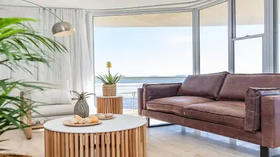 a living room with a brown couch and a table at Lagoon Beach Gem 127 Pool, Views & Sea Breeze in Cape Town