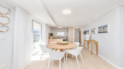 a dining room with a wooden table and white chairs at Lagoon Beach Gem 127 Pool, Views & Sea Breeze in Cape Town