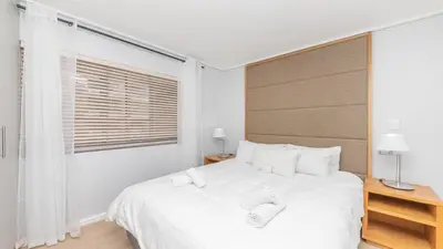 a white bedroom with a large bed and a window at Lagoon Beach Gem 127 Pool, Views & Sea Breeze in Cape Town
