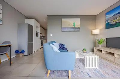 a living room with a blue chair and a tv at Beach Break Bliss - Cozy retreat with mountain views in Bloubergstrand
