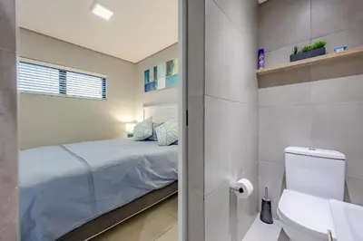 a small bedroom with a bed and a toilet at Beach Break Bliss - Cozy retreat with mountain views in Bloubergstrand