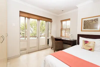 a bedroom with a bed and a desk and windows at The Stellenbosch Hotel in Stellenbosch