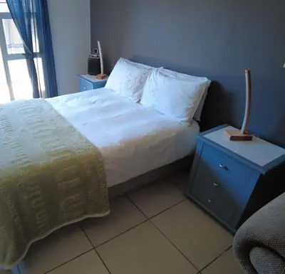 a bed with white sheets and a nightstand with a lamp at Studio Flat Bayside in Cape Town