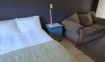 a bedroom with a bed and a couch and a lamp at Studio Flat Bayside in Cape Town