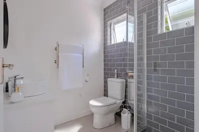 a white bathroom with a toilet and a window at Serenity on 6th Luxury holiday home in Hermanus
