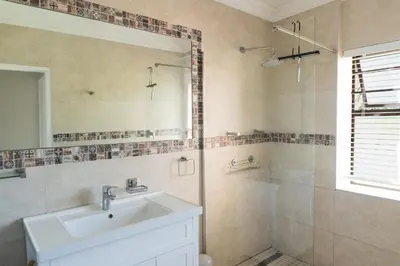 a bathroom with a sink and a shower with a mirror at Begonias Eden in Helderberg