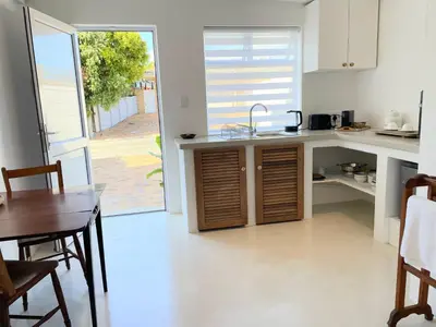 a kitchen with a sink and a table and a door at Spekboom in West Beach in Cape Town