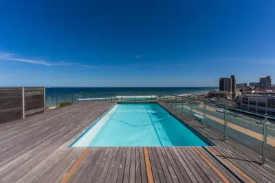 a swimming pool on the roof of a building with the ocean at Stylish 2-Bedroom Sea-View Apartment Horizon Bay Blouberg Beachfront in Cape Town