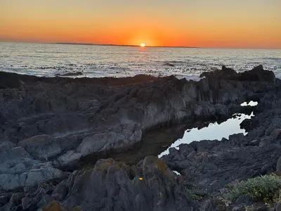 a sunset over the ocean with rocks in the water at Beach Front in Cape Town