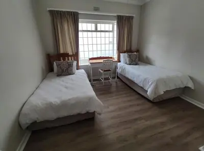 a room with two beds and a table and a window at Voëlklip House - Home with Pool & Mountain views in Hermanus