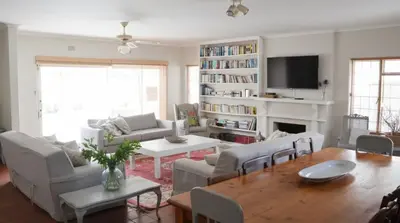 a living room with couches and a table and a tv at Voëlklip House - Home with Pool & Mountain views in Hermanus