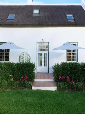 a white house with a door and two umbrellas at Adara Palmiet Valley Luxurious Boutique Farm Hotel in Paarl