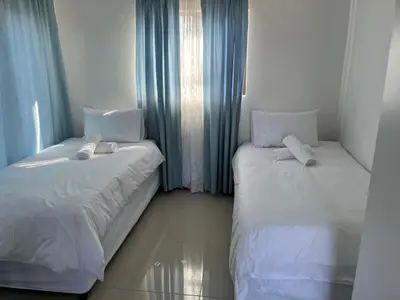 two beds in a room with blue curtains at SNE Travellers in Faure