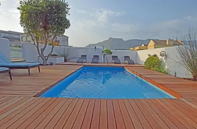 a swimming pool on a wooden deck with chairs on a patio at Apartment Dolphin House in Hermanus