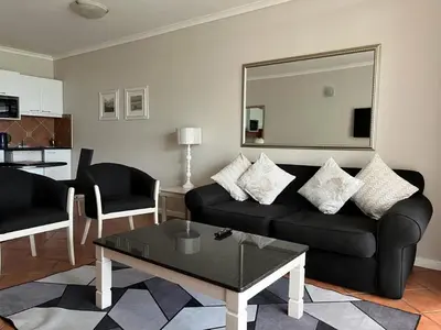 a living room with a black couch and a mirror at Cape Town Beachfront Apartments at Leisure Bay in Cape Town