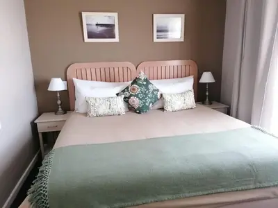 a bedroom with a bed with a green blanket and pillows at Cape Town Beachfront Apartments at Leisure Bay in Cape Town