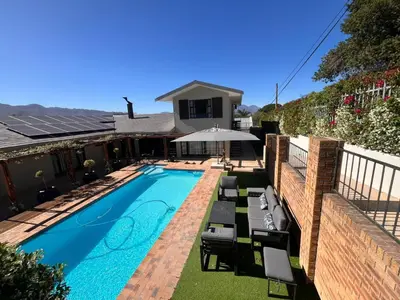 a swimming pool with chairs and an umbrella next to a house at 18 On Louvre Guesthouse in Paarl