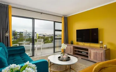 a living room with a blue couch and a flat screen tv at Elegant Two Bedroom Apartment in Century City in Cape Town