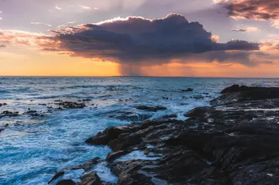 a storm cloud over the ocean with rocks at Ocean View Apartment in Blouberg Beachfront in Cape Town