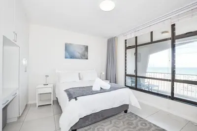 a white bedroom with a bed and a large window at Ocean View Apartment in Blouberg Beachfront in Cape Town