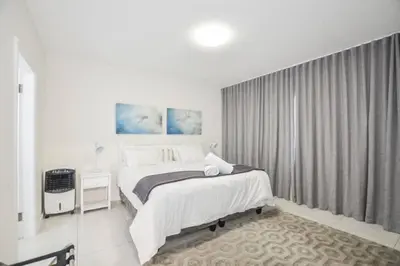 a white bedroom with a bed and a window at Ocean View Apartment in Blouberg Beachfront in Cape Town