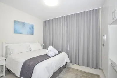 a white bedroom with a bed and a window at Ocean View Apartment in Blouberg Beachfront in Cape Town