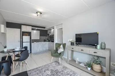a kitchen and living room with a television and a table at Modern 1 Bedroom Apartment in Blouberg in Cape Town