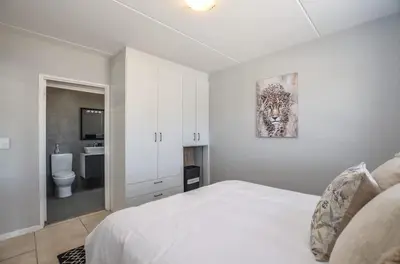a white bedroom with a bed and a bathroom at Modern 1 Bedroom Apartment in Blouberg in Cape Town