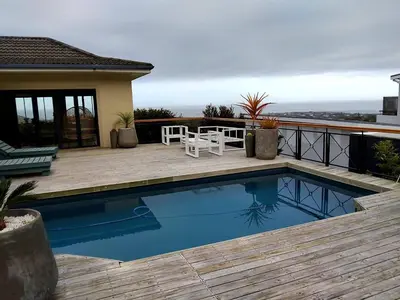 a swimming pool with a table and a chair on a deck at Chanteclair Holiday Home in Hermanus