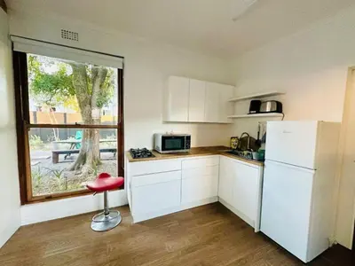 a kitchen with white cabinets and a red stool in front of a window at Stellebosch garden flat in Stellenbosch
