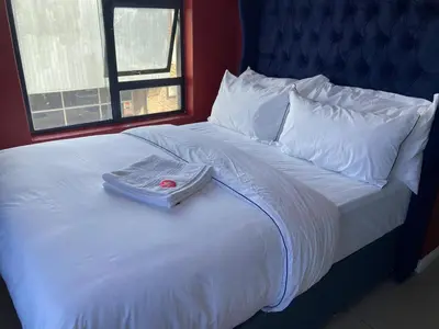 a white bed with a blue headboard and white pillows at Pro Max Guesthouse Goodwood in Goodwood