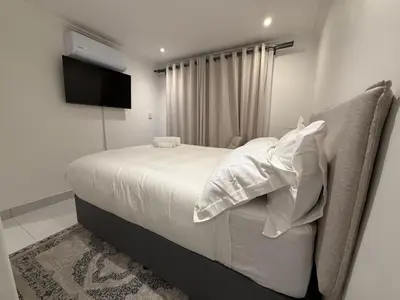 a bedroom with a bed with white sheets and a television at Cherrywood Guest House in Cape Town