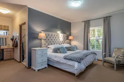 a bedroom with a large bed and a chair at Cheerful 4 bedroom home with pool & wonderful view in Somerset West