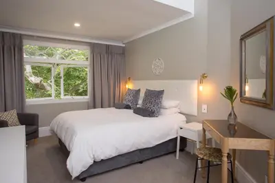 a bedroom with a bed and a desk and a window at Summerwood Guest House in Stellenbosch