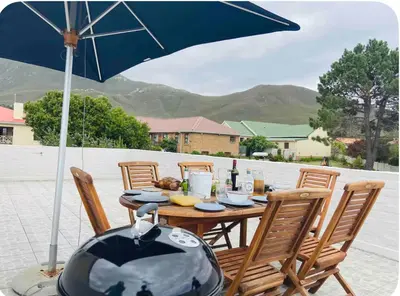 a wooden table with chairs and an umbrella at Fynbos Mountain View in Kleinmond