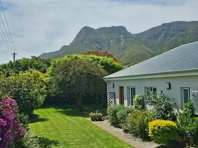 a white house with a garden and mountains in the background at Torbrae Cottage in Hermanus