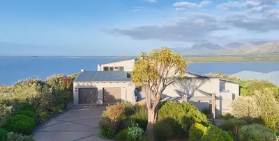 a white house with a tree in front of the water at Exclusive Estate, Panoramic Beauty, Watersports in Lake Marina