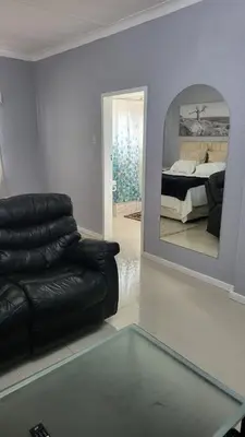 a living room with a black leather couch and a mirror at Vasco Geusthouse in Goodwood