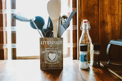 a container of utensils on a wooden table with a bottle at Galileo Farm in Elgin