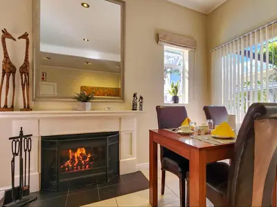a living room with a fireplace and a dining room table and a mirror at Hajo's Lodge & Spa in Cape Town