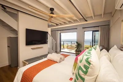 a bedroom with a bed and a large window at Oceanfront Duplex Apartments, Hermanus Waterfront in Hermanus