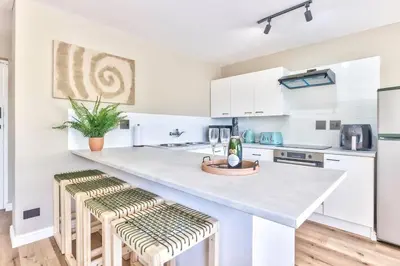 a kitchen with white cabinets and a counter with stools at Silverview Modern Duplex Fully Air-Conditioned near Beach in Cape Town