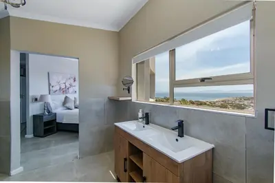 a bathroom with a sink and a window with a bed at 75 on Chapman in Gordonʼs Bay