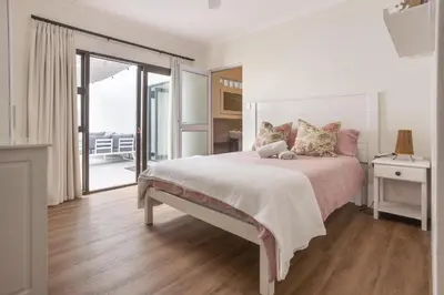a white bedroom with a large bed and a balcony at 5 Bedroom Family Home with Private Apartment in Hermanus