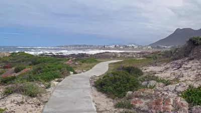 a path on a beach with the ocean and a city at 138 Marine Beachfront Guesthouse in Hermanus