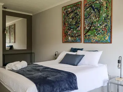 a bedroom with a white bed with a painting on the wall at Sandbaai Breeze in Hermanus